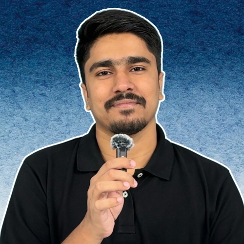 Young man with short dark hair and trimmed beard wearing a black polo shirt, holding a small handheld microphone, positioned against a textured blue gradient background.